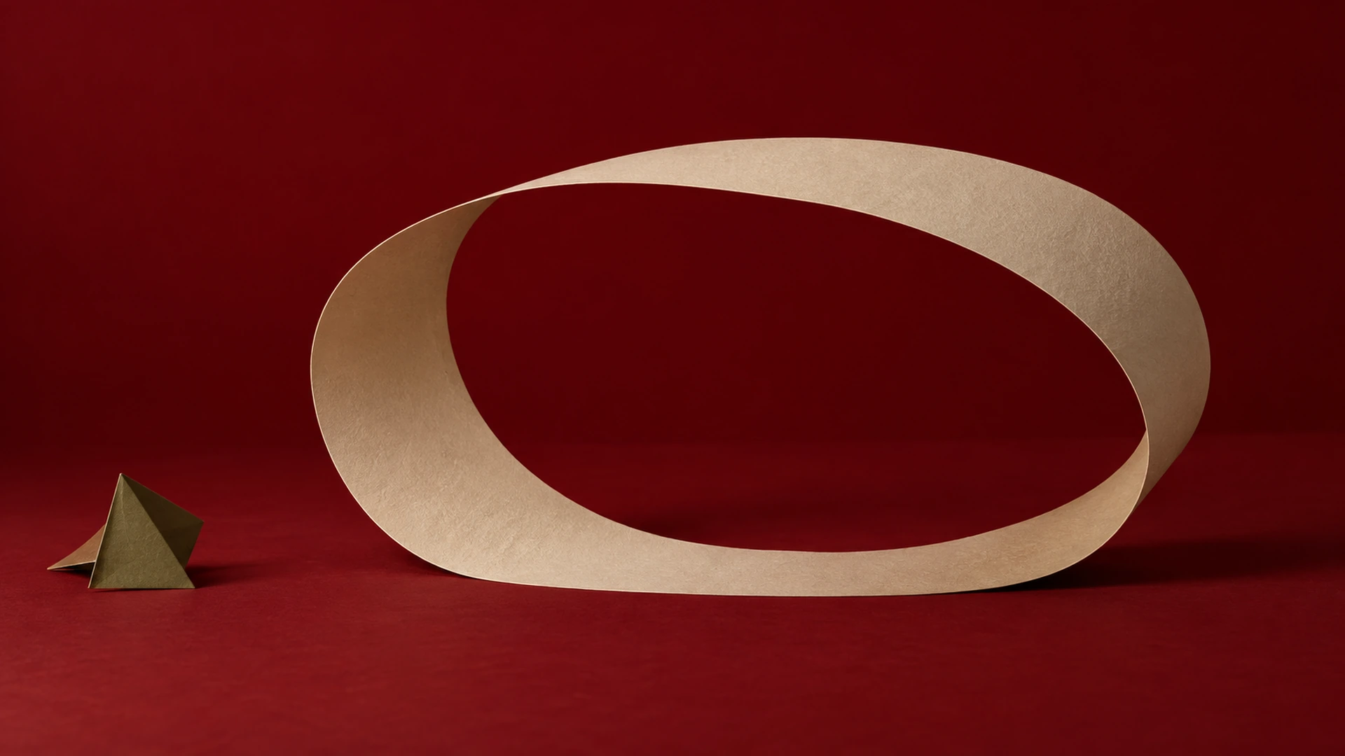 A single champagne paper loop with a generous open center and space around it, against an oxblood backdrop.